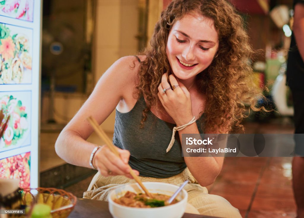 Shot of a young woman eating a bowl of prawn noodle soup in a Vietnamese restaurant