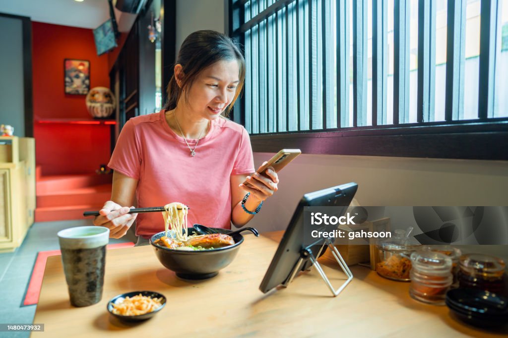 Busy woman eating ramen in restaurant surfing the net with smart phone and digital tablet
Woman eating in restaurant while working with phone and tablet