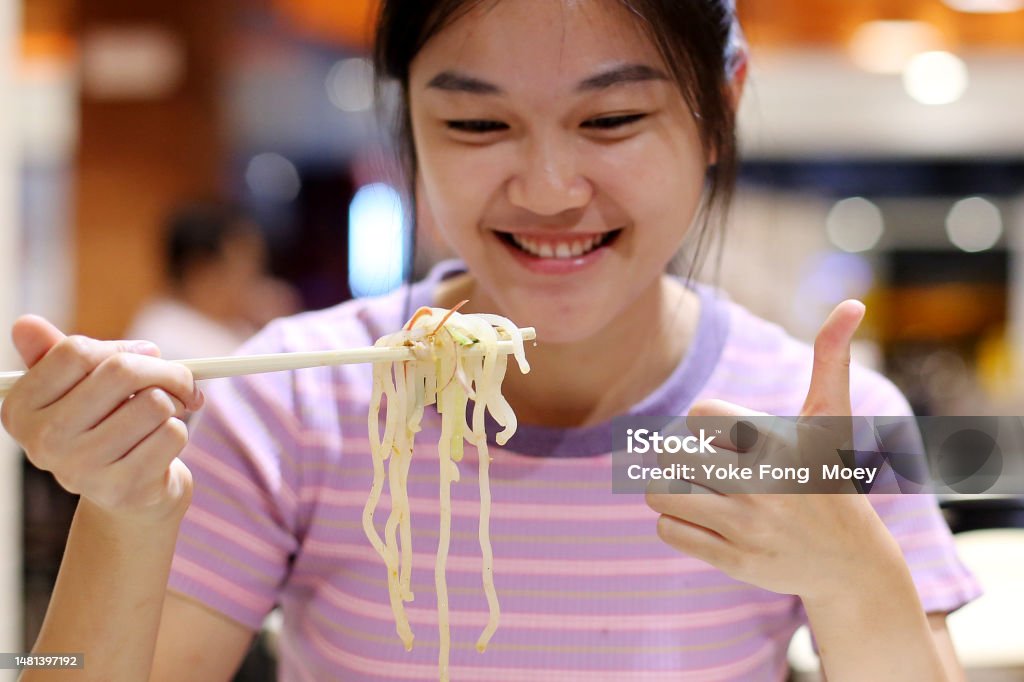 An Asian young woman is enjoying a bowl of Malaysian asam laksa (spicy fish broth noodle) in restaurant
