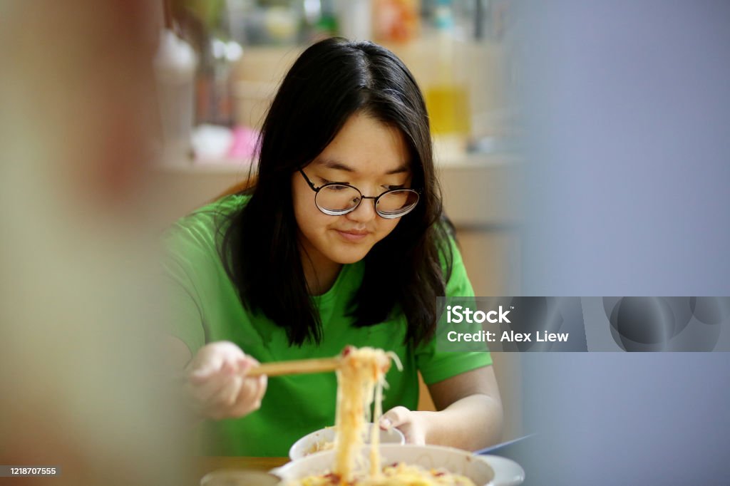A teenage girl is enjoying mealtime while using smartphone for online learning during lockdown in Malaysia.